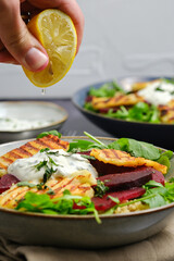 Person Garnishing lemon on Vegetarian Grilled Halloumi Quinoa Salad with Beetroot. Healthy Mediterranean Food Concept.
