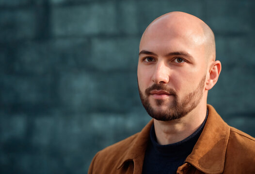 Portrait of a handsome bald man in a brown jacket on a dark background