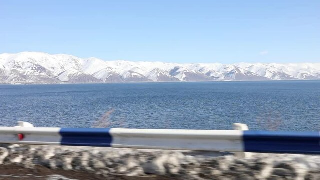 Snow mountain on lake Sevan and blue sky from moving on road car