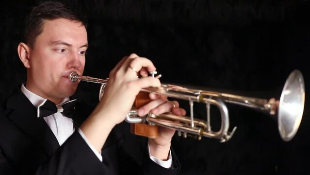 Man in suit and with bow tie plays on a trumpet in a dark room