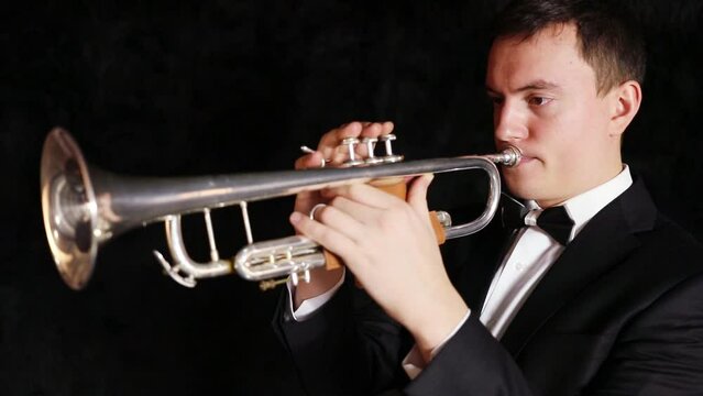 Man is playing on trumpet moving from side to side in a black room