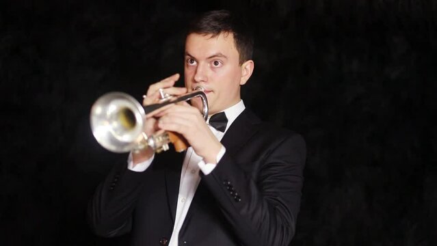 Man in a simple suit plays on a trumpet in a black room