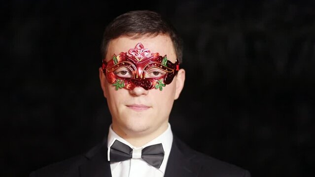 Portrait of a young man in a red carnival mask adjusting a bow tie