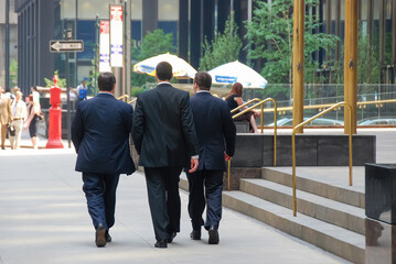 Close up view of three business man in suit seen on the back while walking on sidewalk of Park...