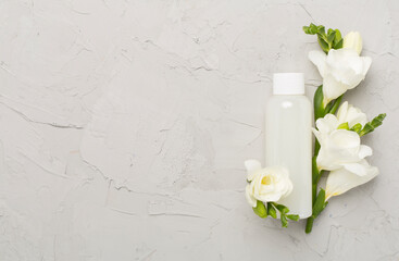 Cosmetic bottle with freesia flowers on concrete background, top view