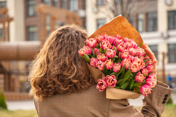 Girl with wavy hair with a large bouquet of pink tulips on the background of a residential building