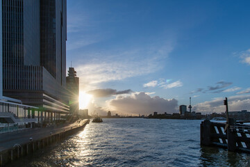 Panoramic view over the Maas river in Rotterdam, The Netherlands with high rise buildings on Holland Amerika Kade on the quay side during sunset with blue sky and clouds