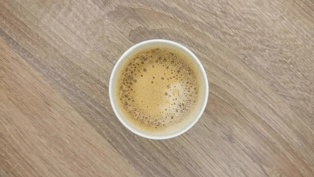 Top view of white paper disposable Irish coffee cup with foam on a wooden table in caffee house.