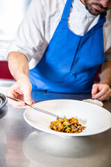 Chef prepara setas de temporada salteadas con yema de huevo curada con salsa de soja y flores decorativas sobre un plato de loza blanco