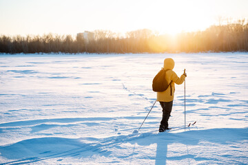 A skier walks on skis in the snow against the background of the setting sun, the glare of yellow...