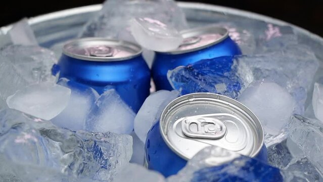 The drink is cooled with ice in a metal can. Beer in aluminum cans was placed in ice. Pieces of ice fall into a container with drinks.