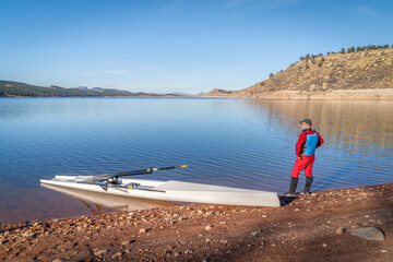 Fototapeta na wymiar Senior male rower and a coastal rowing shell is landing on a rocky shore of Carter Lake in fall or winter scenery in northern Colorado.
