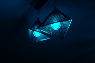 Black and teal hanging dangling triangle ceiling lamp in front of a dark background