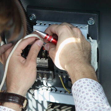 Electrician man in a white shirt with an expensive watch connects wires to a automatic circuit braker switch in a switchboard