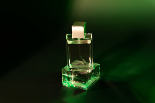 A bottle of perfume stands on a transparent glass stand on a dark green background. Elite perfumes. A scent for the evening. Aroma for a date. Fragrance for Parf maniacs