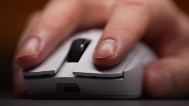 Extreme close-up of unrecognizable man using modern wireless mouse working on computer. Close-up of male finger clicking on white computer mouse on work desk. Shooting in slow motion.