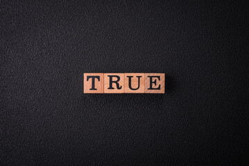 The inscription True made of wooden cubes on a plain background