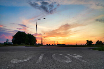Napis stop na drodze asfaltowej o zachodzie słońca.
