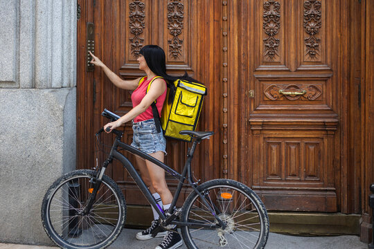 Delivery woman ringing the doorbell with her bicycle
