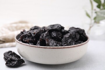 Bowl with sweet dried prunes on light table, closeup