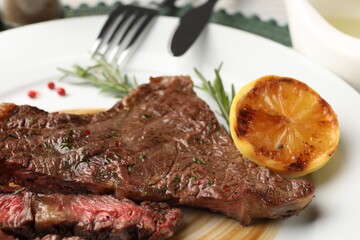 Delicious grilled beef steak with spices and lemon on plate, closeup