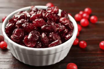Tasty dried cranberries in bowl and fresh ones on wooden table, closeup