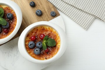 Delicious creme brulee with berries and mint in bowls on white wooden table, top view. Space for text
