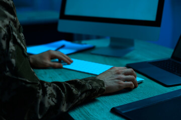 Military service. Soldier working on computer at wooden table in office at night, closeup