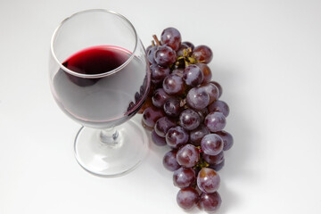 Bunch of grapes with glass of wine on white table. View from above. Clean space for text.