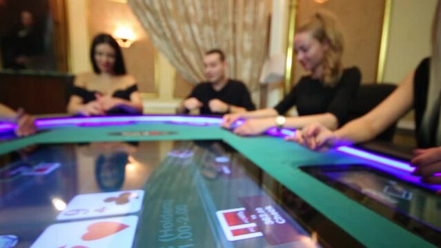 Big screen of electronic poker table and five players (out of focus)