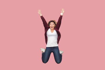 Portrait of excited amazed woman with curly hairstyle jumping up high, looking at camera with big...