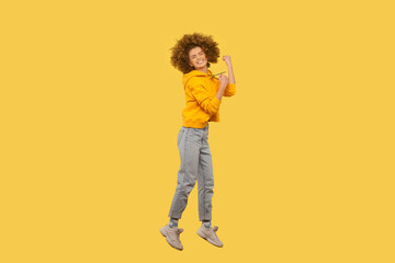 Yes, I did it. Full length portrait of overjoyed woman with Afro hairstyle jumping in the air with...
