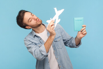 Portrait of happy positive handsome unshaven young man holding in hands paper plane and passport,...