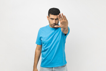 Portrait of unshaven man wearing blue T- shirt standing making stop gesture with his hand, looking...
