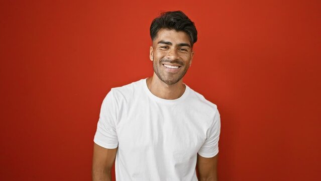 A handsome young hispanic man with a beard in a white t-shirt against a vibrant red background, portraying various expressions.