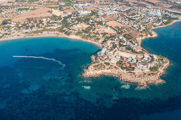 Fototapeta premium Aerial top down view of picturesque village nestled by Cyprus coastline, with azure waters and boats dotting seascape.