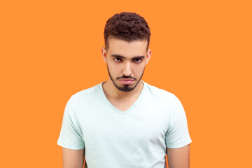 Portrait of sad unhappy young bearded man wearing T-shirt looking at camera with sad upset...