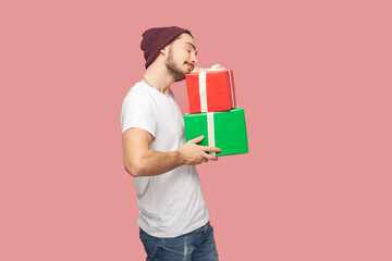 Portrait of satisfied bearded man in white T-shirt and beany hat standing with closed eyes, holding...