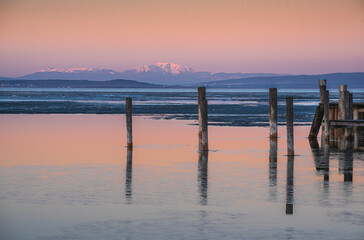 Fototapeta premium Calm water lake with some thin ice and a mountain range covered in snow in the background 