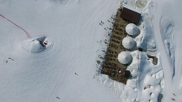 Many people get rest in cafe near end of downhill slope on alpine base