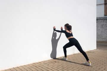 sporty woman doing hamstring stretch against a white wall