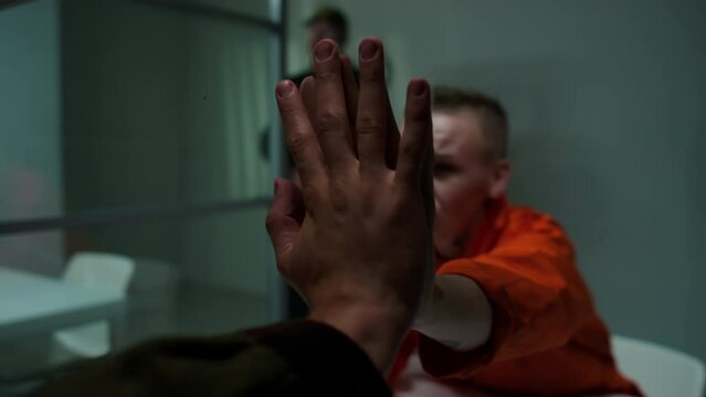 Sad female inmate telling to husband how much she misses him, holding hand through glass and ending phone conversation during visit in prison