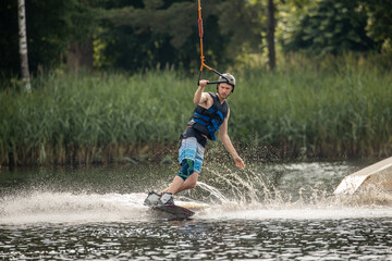 Ypung man wakeboarding and doing different board tricks. Wake boarding sportsman man jumping high wake boarding raley trick with huge water splash in the cable park