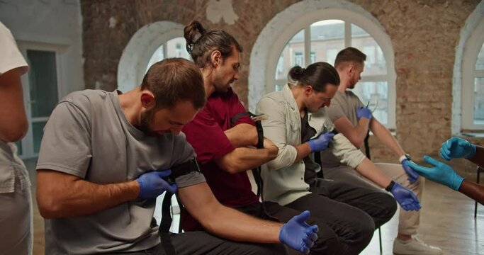Close-up shooting: a group of people learn to work with a medical tourniquet under the guidance of a dark-skinned doctor in a blue medical uniform during a practical medicine class, a professional