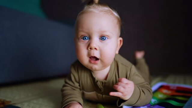 Adorable Caucasian blond baby crawls by the floor. Cute blue-eyed child tries to reach camera.