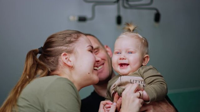 Positive Caucasian parents playing with their little child. Mother kisses her cute baby boy on the cheek. Low angle view.