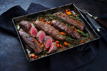 Traditionell gebratenes Rehrückenfilet mit Mangold, Karotten und Kräuter serviert als Nahaufnahme auf einem rustikalen Metall Tablett