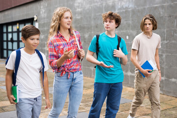 Group of positive cheerful teenagers hanging out on streets of city on summer day