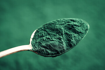 Green spirulina powder on a metal spoon, closeup