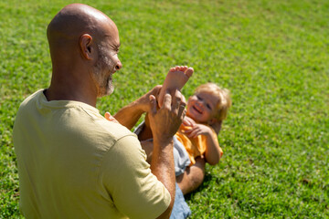 family and love concept - young father tickling his little son in park. dad tickles his son's legs...
